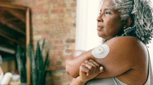 Une femme mûre avec des cheveux gris portant un dispositif de suivi de la glucose continu sur son bras.